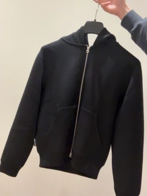 Svart hoodie med dragkedja från j&j - Säljer en svart hoodie med dragkedja framtill och två stora fickor. Perfekt för en chill och enkel stil. Materialet känns mjukt och tjockt, vilket gör den extra bekväm. Oanvänd 