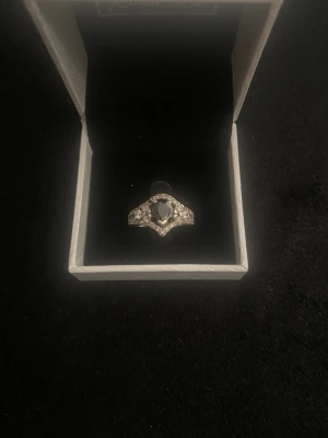 Silverring med svart sten och kristaller - Snygg silverfärgad ring med en stor svart sten i mitten och små gnistrande kristaller runt om. Ringen har en elegant och unik form som verkligen sticker ut. Perfekt accessoar för att lyfta din stil.