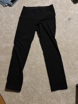 Svarta kostymbyxor från FUNC FACTORY - Snygga svarta kostymbyxor från FUNC FACTORY med klassisk rak passform. Byxorna har diskret knappstängning och är perfekta för en stilren look. Materialet känns mjukt och följsamt, vilket gör dem bekväma att bära hela dagen.