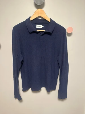 East West tröja  - Mörkblå stickad tröja från East West med klassisk krage och knäppning framtill. Tröjan har lång ärm och är gjord i ett mjukt, värmande material som passar perfekt till kyligare dagar. Enkel och stilren design som är lätt att matcha.