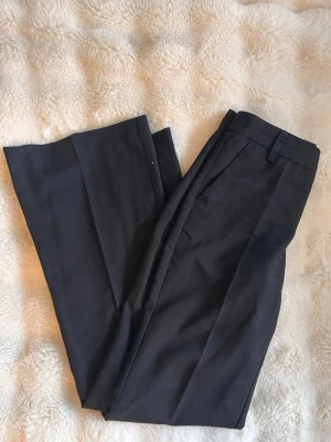 Svarta kostymbyxor från Gina Tricot - Snygga svarta kostymbyxor från Gina Tricot med raka ben och pressveck, bootcut från knäna och ner. Byxorna har hällor för skärp och sidofickor. Perfekta för en clean och stilren look. Materialet känns mjukt och har en lätt stretch. Använda men utan defekter, inga missfärgningar. 