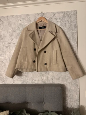Beige dubbelknäppt ullrock Gina Tricot - Kort beige rock från Gina Tricot i använt skick. Jackan är lite nopprig men i annars väldigt bra skick