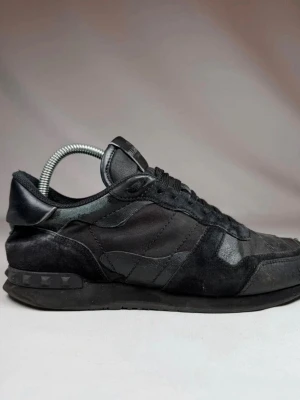 Svarta Valentino rockrunners  - Snygga helsvarta sneakers från Valentino med coola nitar på hälen. Skorna har en mix av mocka och läderdetaljer, samt klassisk snörning och låg profil. Perfekta för dig som gillar stilrena och exklusiva sneakers.