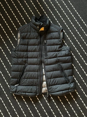 Svart dunväst med dragkedjor - Snygg svart dunväst med ståkrage och quiltad design. Västen har två framfickor med dragkedja och en bröstficka med dragkedja. Stängs med dragkedja och tryckknapp vid halsen. Perfekt lager på lager och riktigt skön att bära.