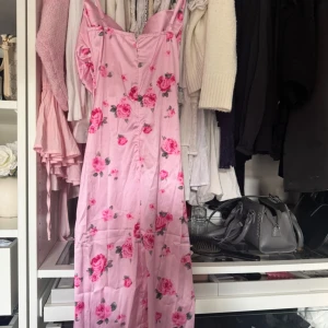 Rosa blommig långklänning med smala axelband - Supersöt långklänning i ljusrosa med blommigt mönster och smala axelband. Klänningen har en figurnära passform och är gjord i ett glansigt satinliknande material. Klänningen är helt oanvänd och är i storlek S!!💞💞