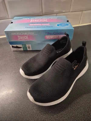 Svarta slip-on sneakers från Skechers - Svarta slip-on sneakers från Skechers med vit sula och stickad ovandel. Skorna har stretchigt material och memory foam-innersula för extra komfort. Har endast använts två gånger 