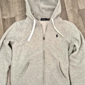 Grå hoodie från Polo Ralph Lauren - Hej! Säljer denna snygga zip-hoodien från Polo Ralph Lauren i storlek M, men passar även S då den är lite mindre i storleken. Köpte den till mitt ex men när vi gjorde slut lämnade han den här, och den kommer inte komma till användning längre. Han hann knappt använda den så den är i toppen skick, hör av er vid funderingar 💞💞Köpte den för 2300kr