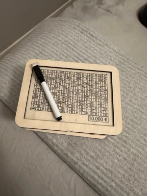 Sparbössa i trä med markeringstavla - Säljer en sparbössa i ljust trä med en markeringsbar tavla på framsidan där du kan fylla i sparade belopp med medföljande whiteboardpenna. Perfekt för att hålla koll på sparmålet, upp till 10 000 euro. Modern och enkel design.