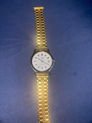 Guld- och silverfärgad Q&Q klocka - Stilren klocka från Q&Q med länkarmband i guld- och silverfärg. Urtavlan är vit med tydliga markeringar och datumvisning. Klassisk rund form och metallarmband som ger en tidlös look.