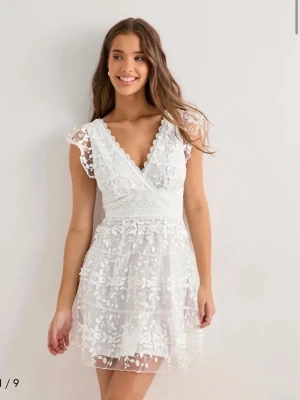 Vit spetsklänning med v-ringning - Superfin vit kortklänning med v-ringning och spetsdetaljer. Klänningen har blommigt mönster, markerad midja och är ärmlös med volangkant. Perfekt för sommarens alla tillfällen och ger en romantisk vibe. Har aldrig använts och behöver bli av med den då returtiden gått ut🤍