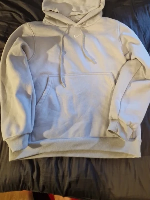 Ljusgrå Nike hoodie - Säljer en ljusgrå hoodie från Nike med klassisk huva och dragsnören. Hoodien har en stor magficka och ribbade muddar vid ärmar och nederkant. Perfekt för en avslappnad och sportig stil.