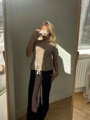 Beige stickad topp med knytband💖💖 - Säljer en beige stickad topp med korta ärmar och rund hals. Toppen har ett dekorativt knytband i midjan som ger en snygg siluett. Materialet är mjukt och lätt, perfekt för lager på lager. Enkel och stilren design som passar till mycket.