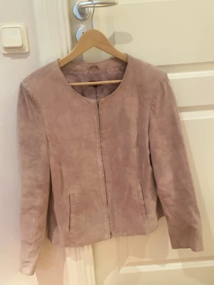 Ljusrosa mockajacka med dragkedja - Snygg ljusrosa mockajacka med rund halsringning och diskret dragkedja framtill. Jackan har raka ärmar och två fickor framtill. Enkel och stilren design utan synliga detaljer eller loggor. Köpt i vintage butik i göteborg