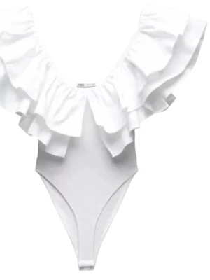 Vit body med volang från Zara - Supersnygg vit body från Zara med breda volanger runt ringningen som ger en trendig och romantisk look. Djup urringning och hög benskärning. Tillverkad i stretchigt material som sitter bekvämt och formar sig efter kroppen. Perfekt till sommarn💗