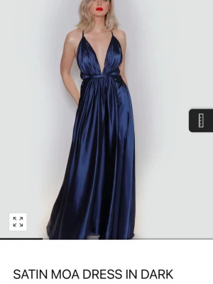 Mörkblå långklänning i satin - Elegant mörkblå långklänning i glansigt satinmaterial med djup v-ringning och smala axelband. Klänningen har en markerad midja och ett svepande fall som ger en lyxig känsla. Perfekt för dig som vill sticka ut på nästa stora event. Från ivoryfield och nästan som ny. Nypris var 2500 kr