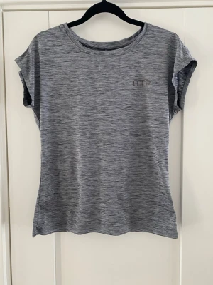 Gråmelerad tränings-tshirt OTF - Snygg gråmelerad t-shirt från OTF med korta ärmar och rund hals. Tillverkad i ett mjukt och lätt material som passar perfekt till träning. Diskret logga på bröstet och söm längs ryggen för extra stil. Använd men i bra begagnat skick   Mått Över bröstet: ca 45 cm Längd från axeln och ner: ca 57 cm  91% polyester och 9% spandex   Kommer från ett djur och rökfritt hem  