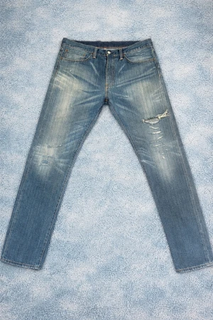 Levi's slitna blå jeans herr - Säljer ett par klassiska blå Levi's jeans med slitningar och distressed detaljer på låret. Jeansen har rak passform, fem fickor och den ikoniska läderlappen bak i midjan. Perfekta för en avslappnad och trendig look. 32:32