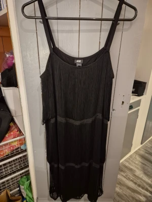 Svart fransklänning från H&M - Cool svart klänning från H&M med tunna axelband och långa fransar som ger en riktigt snygg och unik look. Klänningen har en rak passform och är perfekt för dig som vill sticka ut. Materialet känns lätt och flowy.