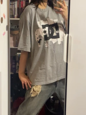 Grå oversized DC t-shirt - Säljer en grå oversized t-shirt från DC med stort svart och vitt logotryck på bröstet. 