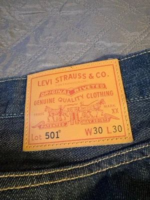 Levi's 501 blå jeans W30 L30 - Klassiska blå Levi's 501 jeans med rak passform och fem fickor. Jeansen har den ikoniska läderlappen bak i midjan och är tillverkade i slitstark denim. Perfekta för dig som gillar tidlös stil och vill ha ett par riktigt snygga jeans.
