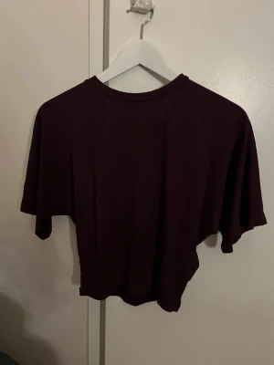 Mörkröd croppad t-shirt - En enkel och stilren mörkröd croppad t-shirt med korta ärmar och rund hals. Perfekt till jeans eller kjol för en avslappnad look. Materialet känns mjukt och skönt mot huden.