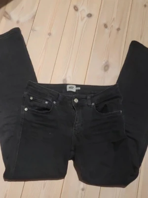 Svarta raka jeans med silverknappar - Säljer ett par svarta jeans med raka ben och klassisk femficksdesign. Jeansen har silverfärgade knappar både fram och på bakfickorna. Märket är 157 och materialet känns som bomull med lite stretch. Perfekta till en avslappnad look.