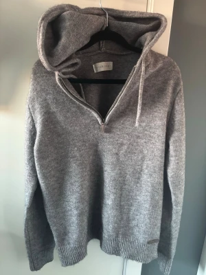 Grå stickad hoodie från pier one - Skön grå stickad hoodie från pier one med dragkedja framtill och justerbar huva med snören. Tröjan har ribbade muddar vid ärmslut och nederkant, perfekt för en avslappnad och stilren look. Materialet känns mjukt och värmande.