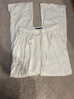 Vita linnebyxor - Säljer ett par vita linnebyxor från lager med avslappnad passform. Byxorna har resår i midjan med snören , sidofickor och en bakficka. Perfekta för en chill och stilren look. Materialet är lätt och luftigt linne. Dem är genomskinliga 