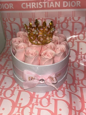 Evighetsrosor i presentbox - Lyxig rund presentbox  fylld med ljusrosa rosor och dekorerad med en guldfärgad krona med pärlor. Boxen har ett rosa band  och en liten rosett framtill. Perfekt som exklusiv gåva eller dekoration.