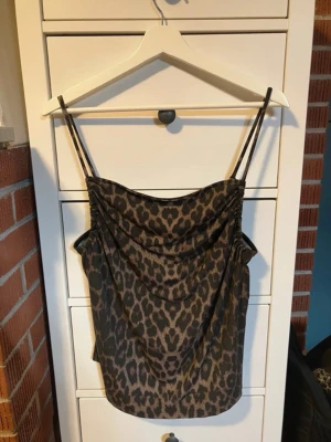 Leopardmönstrad linnetopp med tunna band - Säljer en snygg leopardmönstrad linnetopp med tunna axelband och draperad front. Toppen har en loose passform och är perfekt för dig som vill sticka ut. Materialet känns mjukt och följsamt, troligen polyester. Perfekt att styla med jeans eller kjol.