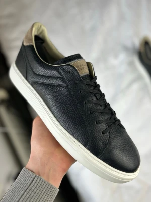 Svarta sneakers från Brunello Cucinelli - Stilrena svarta sneakers i premiumläder från Brunello Cucinelli. Skorna har vita sulor, svarta skosnören och beige detaljer vid hälen. Klassisk låg modell med diskret logga på plösen och snygg textur i lädret.