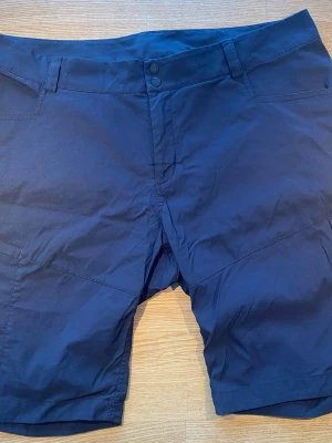 Svarta shorts från Peak Performance XL - Peak Performance Whirl Light friluftsshorts för dam i storlek XL. Färg svart. Tillverkade i polyester enligt tvättrådslappen. Modellen har bälteshällor i midjan, knapp- och gylfstängning samt flera fickor. Passar för vardagsbruk och friluftsaktiviteter där lätta och funktionella shorts önskas.  Endast använda vid ett par tillfällen och är i väldigt fint begagnat skick   Mått Över midjan: ca 47 cm Längd från grenen och ner: ca 24 cm  96% polyester och 4% elastan   Kommer från ett djur och rökfrit