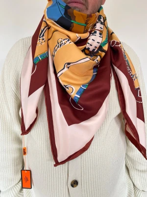 Färgstark H ermes silk sidenscarf - Säljer en lyxig sidenscarf från H ermes med färgstarkt mönster i vinrött, beige, gult, blått och grönt. Scarfen har klassiska kedje- och remdetaljer och kvadratisk form. Perfekt accessoar för att lyfta din outfit. %100 silk 
