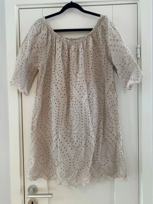 Beige broderad kort klänning - Luftig beige kort klänning med broderade detaljer och hålmönster. Klänningen har offshoulder-modell med resår vid halsringningen och halvlånga ärmar. Perfekt för varma dagar och ger en romantisk vibe. Endast använd vid ett par tillfällen och är i fint begagnat skick  Mått Över bröstet: ca 59 cm Längd från axeln och ner: ca 88 cm   100% bomull  Kommer från ett djur och rökfritt hem
