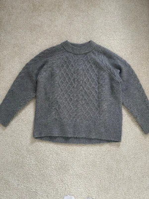 Grå stickad tröja - En grå stickad tröja med kabelstickat mönster framtill från lager 157. Jättefint skick.