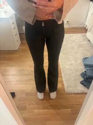 Svarta skinnbyxor från Nelly - Snygga svarta kostymbyxor från Nelly med raka ben och pressveck. Byxorna har fickor fram och stängs med knapp och dragkedja. Perfekta för en stilren look och passar till många olika outfits. Den är använd 1 gång så är helt nya.