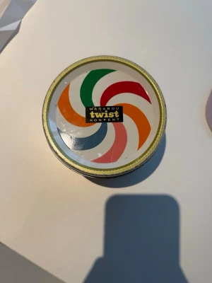 Retro Marabou Twist plåtburk - Säljer en retro plåtburk från Marabou Twist Konfekt med färgglatt mönster i grönt, rött, orange och blått. Burken är rund med lock och har klassisk vintagekänsla, perfekt för samlare eller som dekoration.