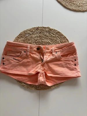 Persikofärgade diesel shorts 39 midjemått  - Snygga persikofärgade shorts med fem fickor, bälteshällor och coola nitar vid fickorna. Klassisk knapp- och dragkedjestängning framtill. Perfekta för varma dagar och ger en fräsch look.