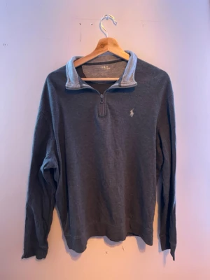 Grå halvzip från Polo Ralph Lauren - Mysig grå långärmad tröja från Polo Ralph Lauren med halv dragkedja och klassisk broderad logga på bröstet. Tröjan har en hög krage med ljusare insida storlek L men passar mer en M