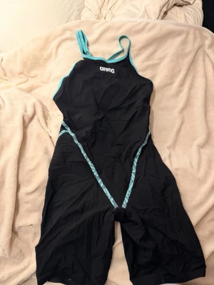 Primo tävlingsbaddräkt från Arena - Säljer en svart tävlingsbaddräkt från Arena med turkosa detaljer och mönstrade sömmar. Baddräkten har långa ben och smala axelband, samt en öppen rygg för extra rörelsefrihet. Perfekt för simträning eller tävling.Arena primo tävlingsbaddräkt mycket väl använd har tydliga tecken på användning men fortfarande i bra skick. Baddräkten är i stl 30 vilket blivit för stort för mig. Nypris 5000-6000kr