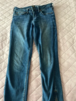 Blå skinny jeans med dragkedja Lee - Snygga blå skinny jeans från Lee med klassisk femficksmodell och dragkedja vid benslutet. Jeansen har en tvättad look och smal passform som sitter tight hela vägen ner. Perfekta för dig som gillar en modern och stilren stil.