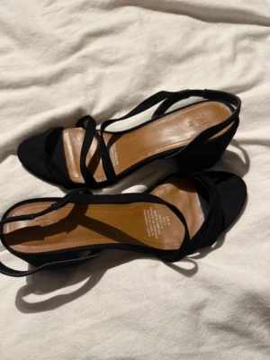 Svarta sandaletter med blockklack - Stilrena svarta sandaletter från H&M med tunna remmar och öppen tå. Skorna har en bekväm blockklack och innersula i brunt konstläder. Perfekta för dig som gillar enkel men trendig design.
