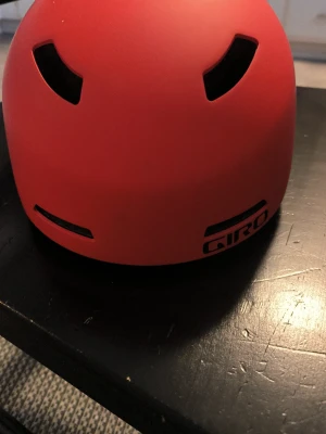 Röd hjälm från Giro - Snygg röd hjälm från Giro med flera ventilationshål och matt finish. Hjälmen har en rundad form och är tillverkad i tålig plast, perfekt för cykling eller skateboard. 