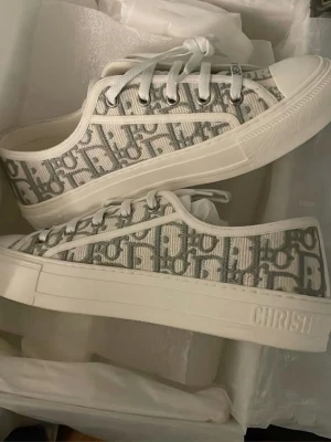 Dior Oblique sneakers - Snygga låga sneakers från Dior med det klassiska gråa och vita Oblique-mönstret. Skorna har vita snören, vit sula och detaljer med Dior-logga på sidan. Tillverkade i canvasmaterial med gummisula för en clean och trendig look. Perfekt inför sommaren🤗