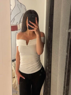 Vit offshoulder topp med v-ringning - Säljer en snygg vit offshoulder topp med v-ringning och åtsittande passform. Toppen är ärmlös och har en stilren, enkel design som passar perfekt till många olika outfits.