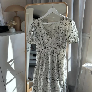 Vit prickig långklänning  - Söt vit långklänning med svarta prickar och v-ringad hals. Klänningen har puffiga korta ärmar och markerad midja. Svarta prickar. Knappt använd. Passar större och mindre. Inte struken på bilden!!