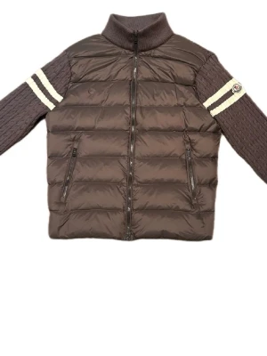 Grå moncler cardigan  - Snygg grå cardigan  från Moncler med stickade ärmar och vita ränder vid överarmarna. Jackan har hög krage, två dragkedjefickor fram och Moncler-logga på ena ärmen. Kroppen är quiltad och vadderad medan ärmarna är kabelstickade för en unik look.