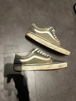 Gråa Vans Old Skool sneakers - Klassiska Vans Old Skool sneakers i grått med vit sula och vit sidostripes. Skorna har lågt skaft, vita snören och är tillverkade i canvas och mocka. Perfekta för en avslappnad streetwear-look.