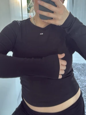 Svart långärmad topp Tommy Jeans - Svart ribbad långärmad topp från Tommy Jeans med liten broderad logga på bröstet. Tight passform och rund halsringning. Perfekt basplagg för alla tillfällen och enkel att matcha med olika stilar.