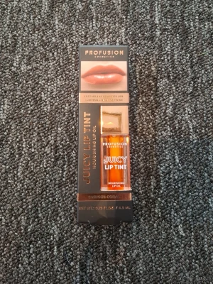 Juicy Lip Tint från Profusion - Juicy Lip Tint från Profusion Cosmetics i färgen Curious Coral. Ett närande läppglans med oljebaserad formula som ger glansig finish och en hint av korallfärg. Kommer i en genomskinlig plastförpackning med gulddetaljer och applikator. Köpt på normal